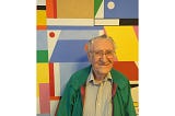 Portrait of an elderly man in a green jacket in front of a bright abstract painting.