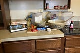 Kitchen counter covered with baking materials and a stack of old cookbooks, illustrating reading to learn to cook rather than being taught by another person.