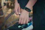 Person adjusting their running shoes while wearing a fitness tracker