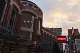 A brick, circular, windowed facade against a cloudy, sunny morning dawn.
