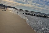 A picture I took of the gentle waves caressing the smooth sand as the sun starts to set in the evening, behind fluffy clouds