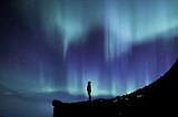 The silhouette of a person gazing up at the aurora borealis