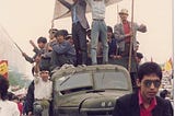 Some Chinese workers atop a truck holding up the sign “工人来了！” (“The workers are here!”) during the 1989 Tiananmen protests.