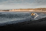 Photograph of a small concrete bunker on a beach being lapped by waves.