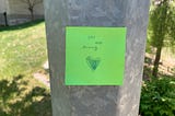 Lime green sticky note on a light post saying, “You are strong.”