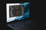 An apple laptop in a dark room with vscode running