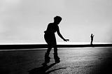 a black and white photo of a skating woman with a man standing in the background