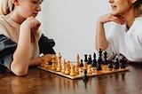 Two young women looking at a chessboard on a table between them