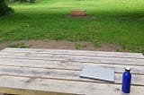 A closed laptop and a water bottle on a picnic bench in a park