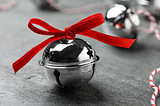 A silver sleigh bell with a red ribbon on a grey table