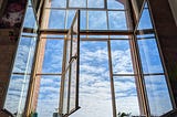 An enormous open window set into exposed brick with plants in the sill