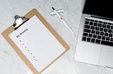 A clipboard, an open pen and an open laptop placed on a table