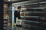 A man stands in front of a refrigerated grocery display, examining items carefully as he decides what to buy.