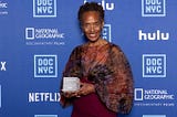 Marcia Smith posing with her Lifetime Achievement Award against a blue-branded DOC NYC step-and-repeat.