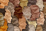 Crinkled paper silhouettes of people’s faces overlap with one another in different shades of color representing a wide range of skin tones.