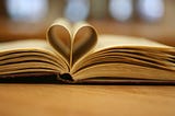 A book lies open with the middle pages gently folded into a heart shape.