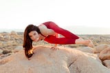 A woman in red sports attire on a rock in the desert doing a yoga pose.