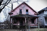 A worn suburban house with peeling paint and a sagging porch.
