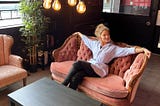 Author is sitting on a light red fabric couch in a lobby in a Thailand hotel