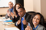 four people clapping and smiling with one giving the thumbs up