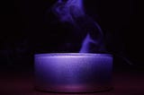 close up color photograph of a blue candle emitting willowy smoke against a black background