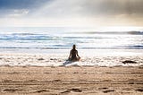 Woman sitting on the beach on a cloudy day. The sun is shining on her.