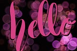 Pink “hello” in brush lettering layered over bokeh in varying shades of pink and purple and a black background.