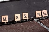 Scrabble tiles seemingly spelling out the word “MISSING,” though the two “I” tiles are missing.