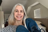 Woman in a bedroom smiling and holding up a pair of blue sneakers
