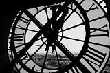 Black and white photo of inside a clock tower, behind the face of the clock with Roman numerals.