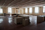 An abandoned, somewhat eery office interior with empty desks, no chairs and dim lighting.