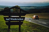 A car driving past a sign that reads Auf Wiedersehen