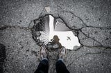 Image of a puddle reflecting skyscrapers and an airplane