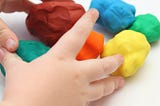 child’s hands playing with playdough of different colors.