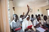 Grade 8 girls in Kenya raise their hand in class discussion while holding their tablets to learn.