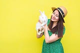 A smiling woman in a green patterned dress holds a white rabbit