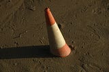 An orange and white traffic cone partially submerged in mud, tilting at an angle.