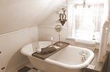 antique claw foot bathtub with chandelier hanging above , bath tray, candlest