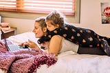 Inside a bedroom, a mother and child laying down on a bed using a laptop.