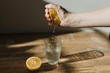 Hand squeezing half an orange into a glass of water