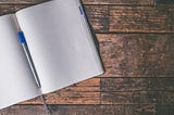 A blank, open notebook with a blue capped pen on a wooden table.