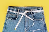 Measuring tape and jeans on a bright yellow background