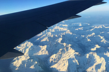 The wing of a plane flying over snowy mountains.