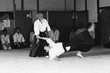 O Sensei is demonstrating an Aikido technique in front of his students