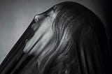 A black white photo shows a woman screaming under a see through veil.