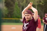A young athlete with Downs syndrome stretches his armss over his head befor a softball match
