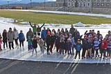 Photo of several World Ice Skating Day participants standing on the outdoor Olympic Speed Skating Oval and smiling.