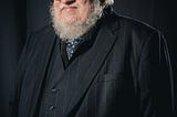 A photograph of George R.R. Martin in a suit. Attribution: Henry Söderlund, CC BY 4.0 <https://creativecommons.org/licenses/by/4.0>, via Wikimedia Commons