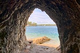 A view through the opening of a cave onto a beach and blue-green sea.