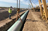 pipe being put into the ground guided by a man is a bright yellow vest